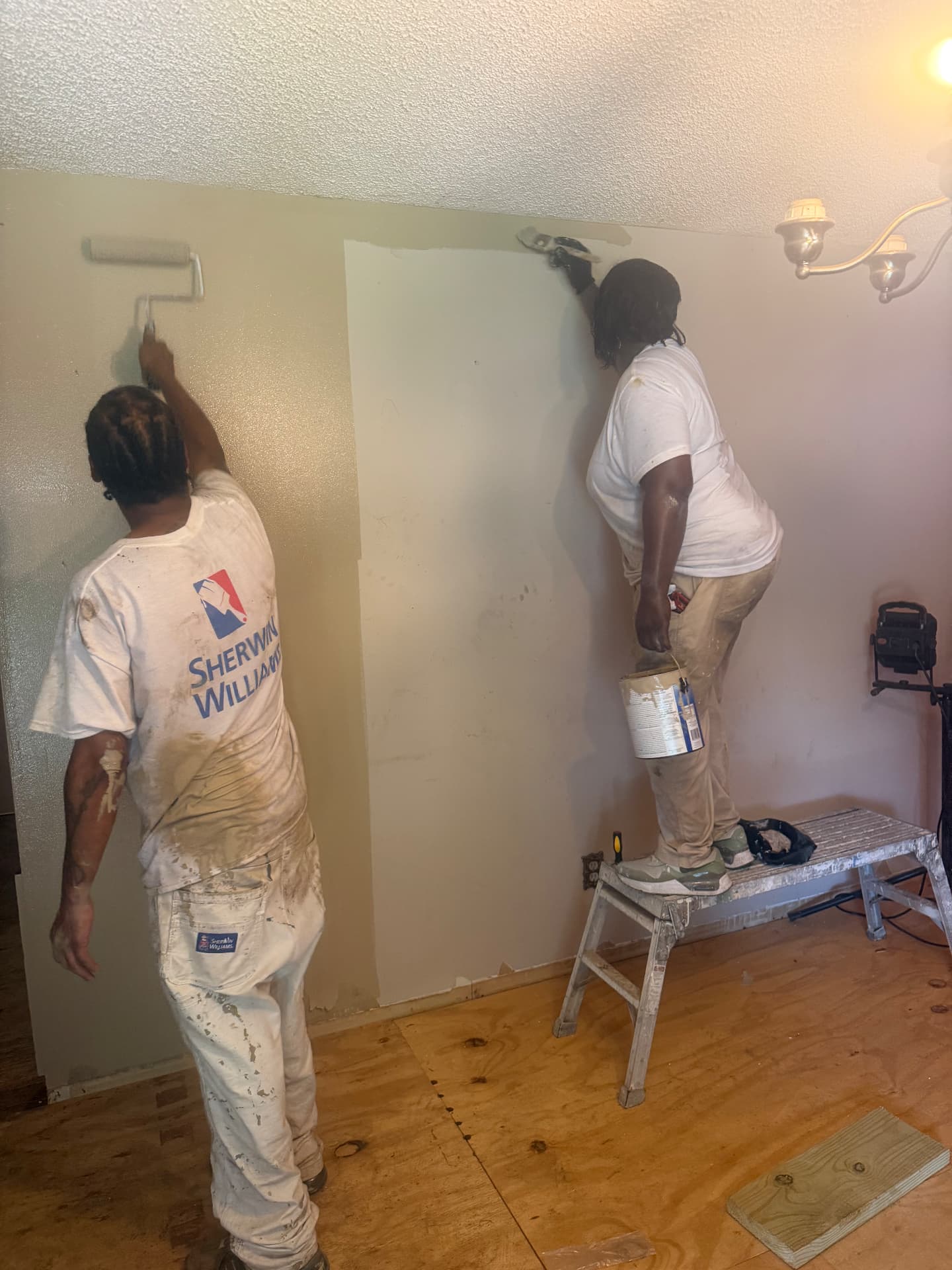 Student cutting in a ceiling line while a teammate rolls the adjoining wall