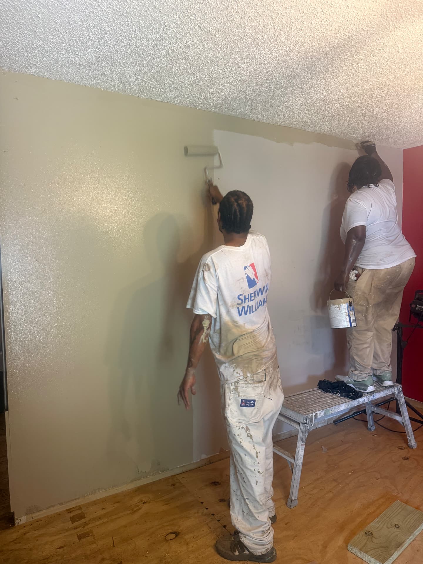 Two students rolling and cutting in fresh wall paint on a residential job site
