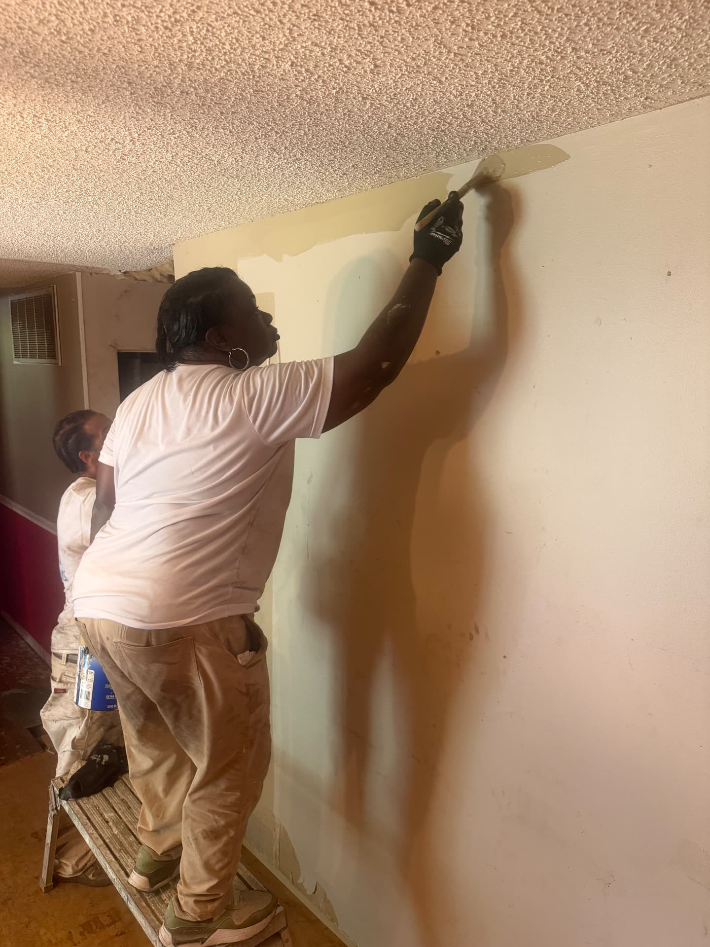 Student brushing paint along a ceiling edge with a trim brush